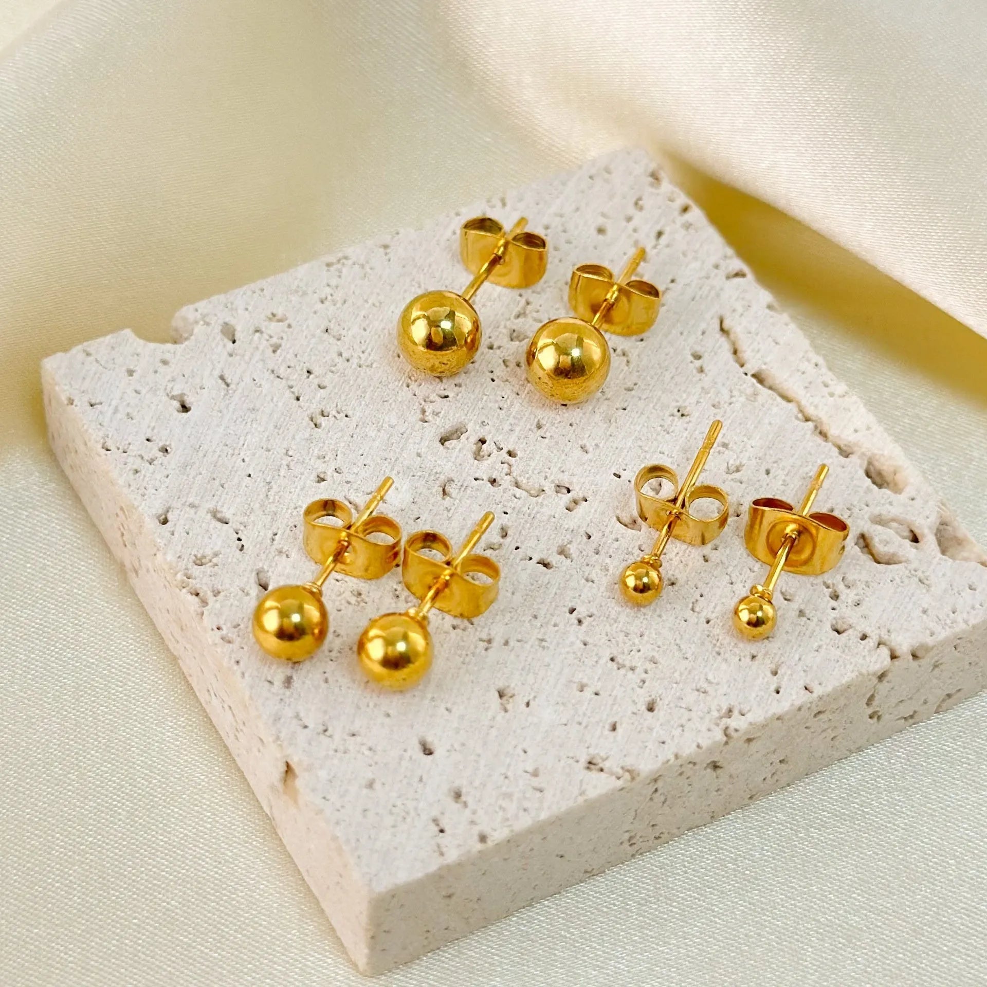 Stainless steel minimalist ball stud earrings with a round geometric shape, shown in various sizes.