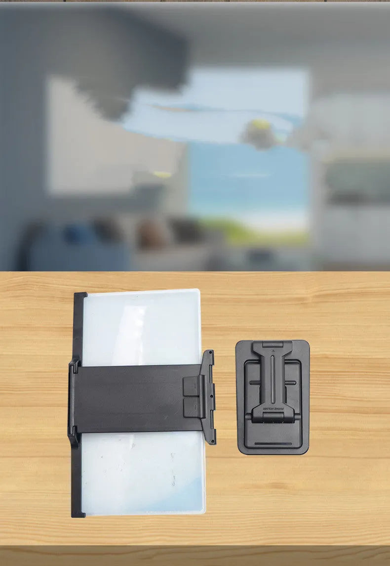 Black detachable mobile phone screen magnifier and holder set up on a desk, showing a phone displaying a magnified movie scene.