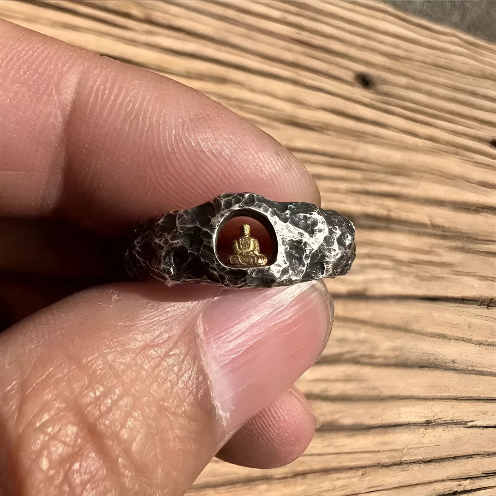 Close-up of a hand-forged copper ring with a Buddha motif and rock texture band on a size 8 finger.