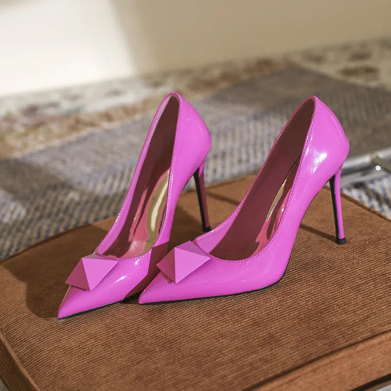 Pink women's pointed toe stiletto high heels with buckle detail on patent leather upper.