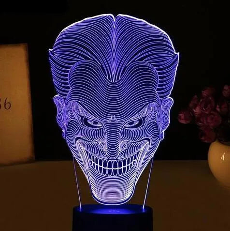 A 3D LED table lamp displaying multiple colours, with a remote control and USB cable on a desk.