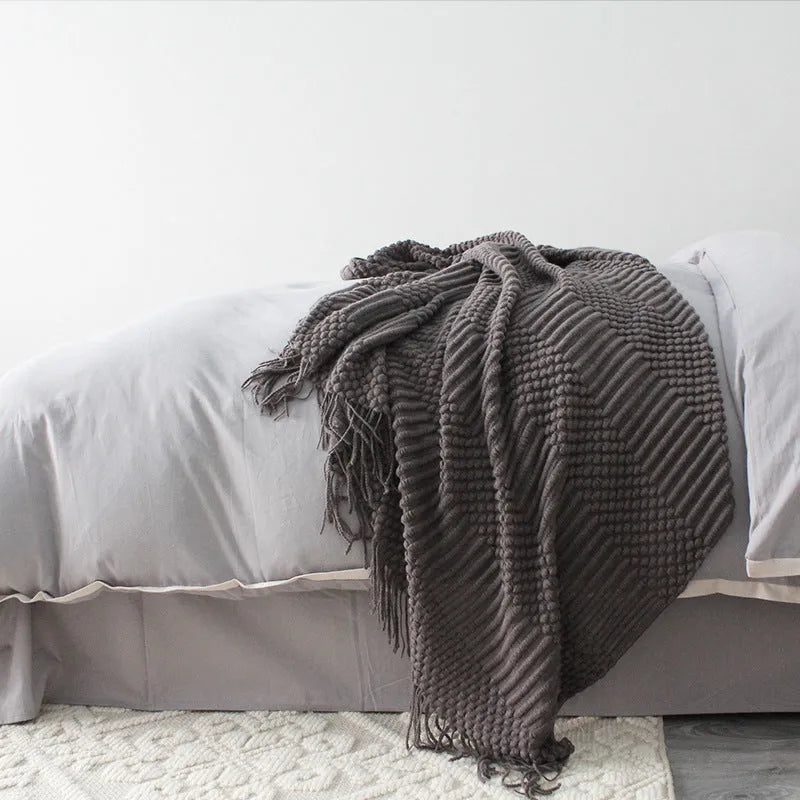 Small grey polyester nap blanket folded on a sofa, showing its size and texture.