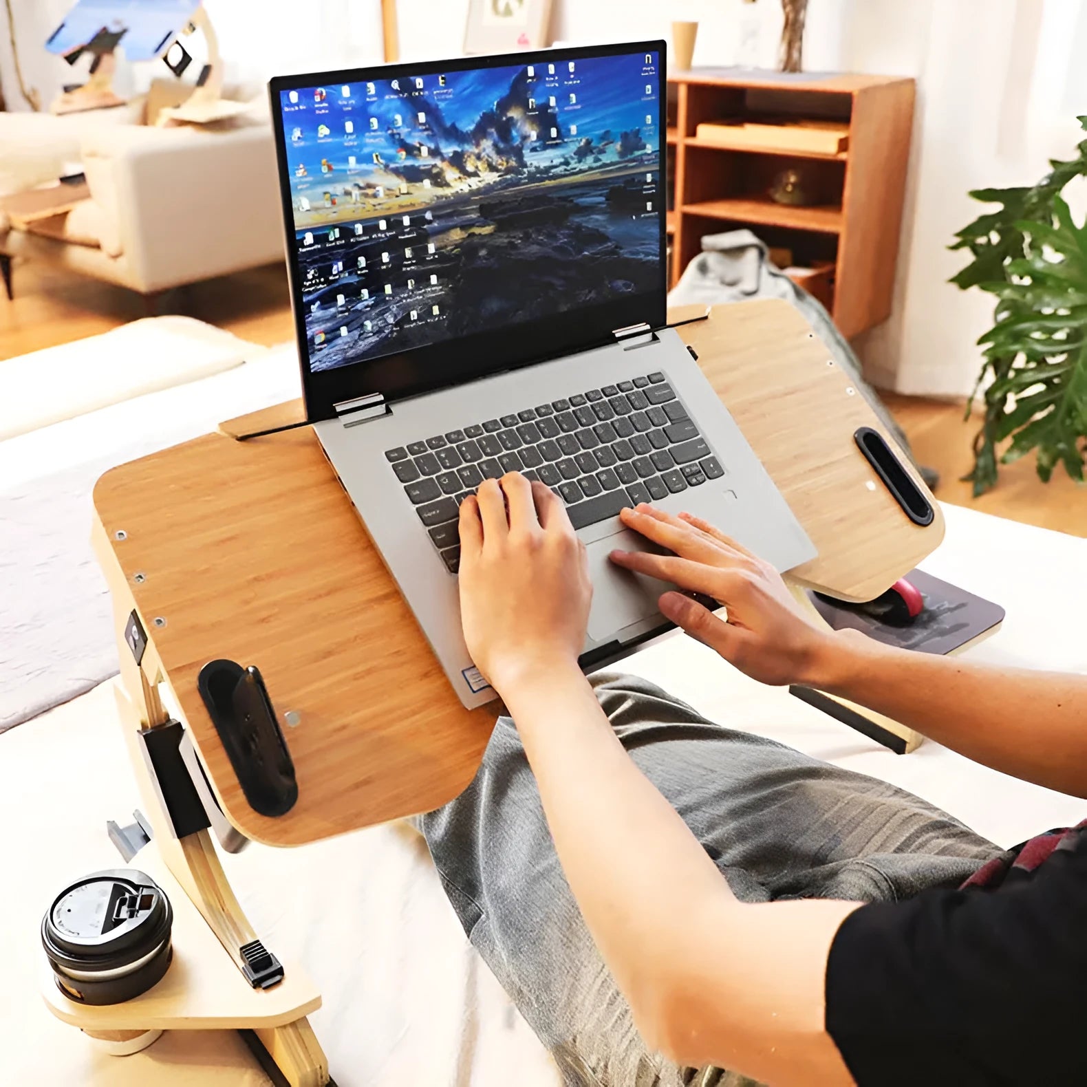 Wooden folding computer table with adjustable angle, shown in black finish on a bed.