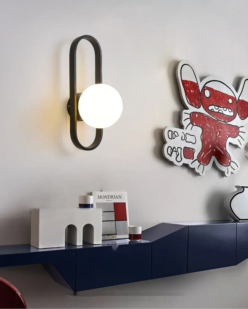Minimalist black iron wall lamp with a glass shade mounted on a white wall.