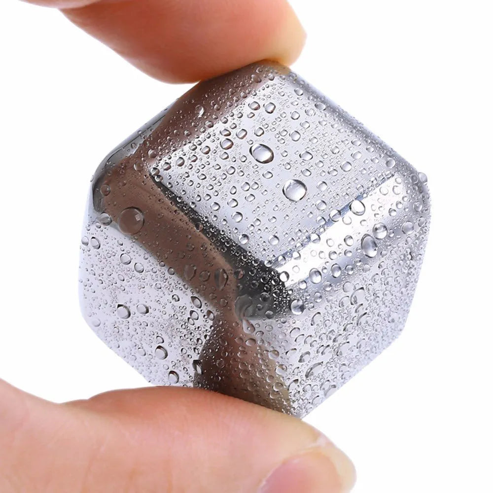 Set of stainless steel reusable whiskey stones in various shapes with metal tongs on a wooden surface.