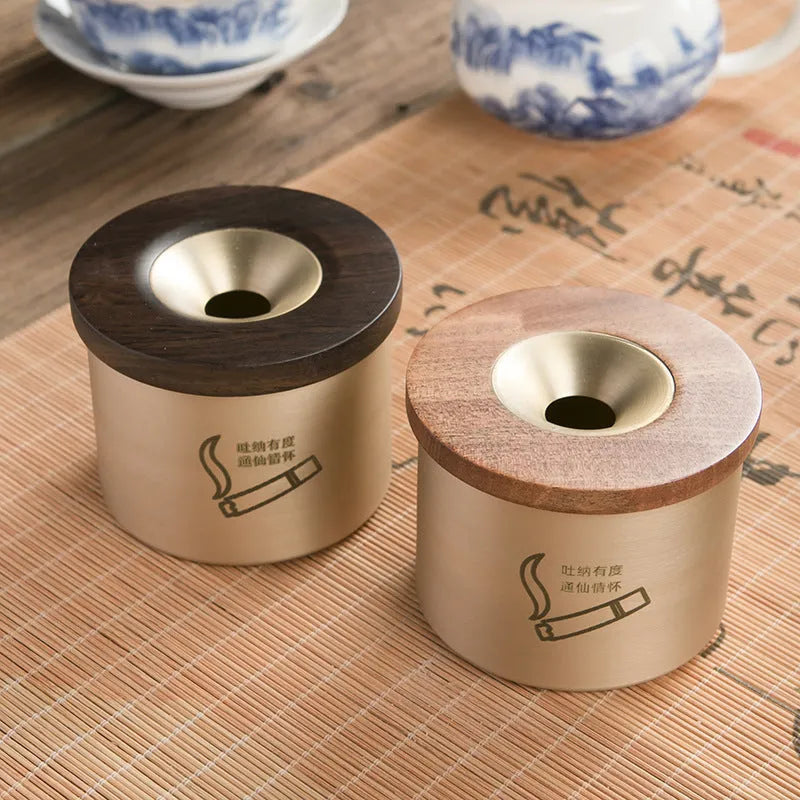 Brass-coloured copper ashtray with a wooden lid on a tabletop.