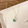 Women's necklace with coloured glaze joker pendant on a beige cotton linen clavicle chain.