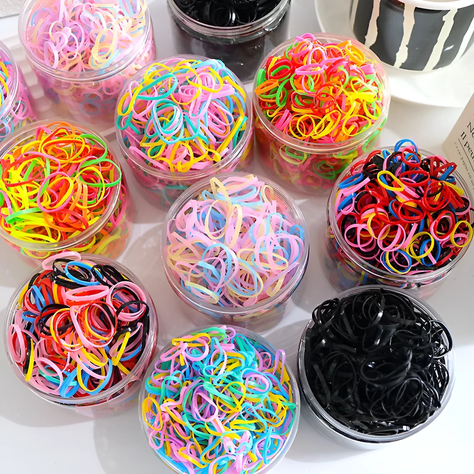 Assorted colourful TPU baby hair ties in a reusable plastic container.