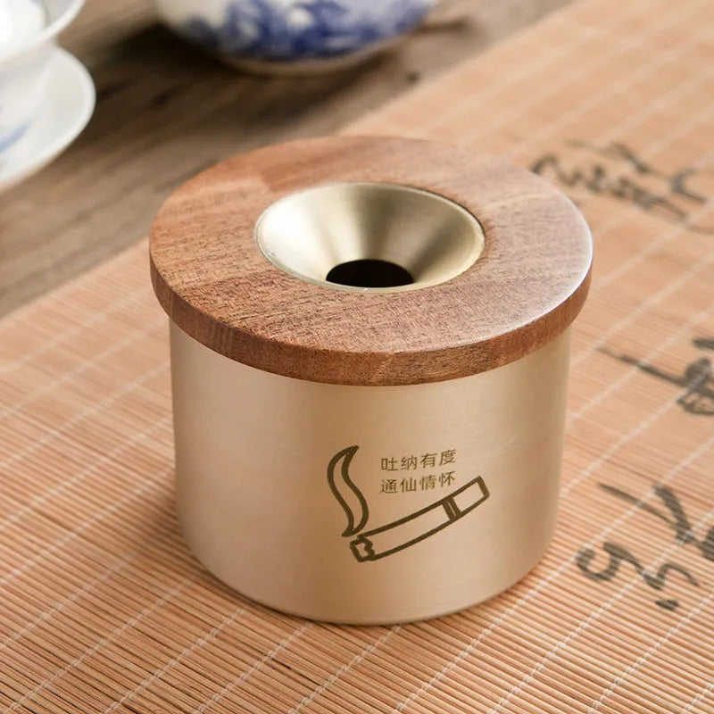 Brass-coloured copper ashtray with a wooden lid on a tabletop.