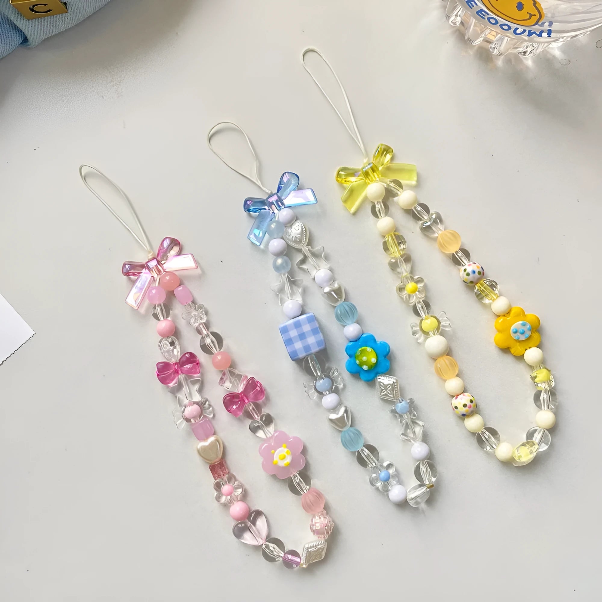 Colourful beaded flower lanyard for mobile phones with blue, pink, or yellow plastic flowers on an adjustable rope strap.