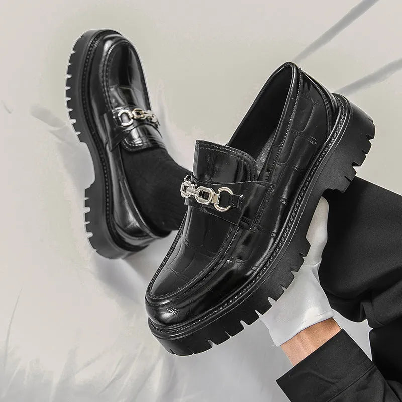Men's black crocodile pattern loafers with a flat platform sole on a plain background.