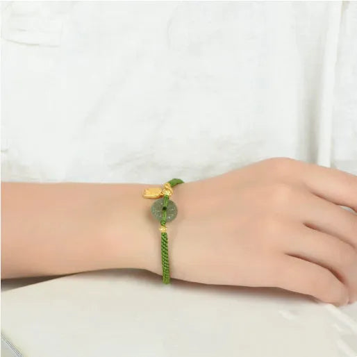 Close-up of a women's hand-woven green rope bracelet with a Hetian jade peace buckle charm.