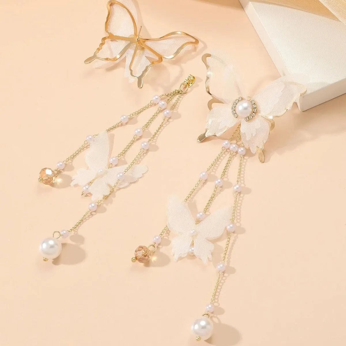 A pair of white butterfly-shaped earrings with pearls, rhinestones, and lace tassels on a copper alloy base.