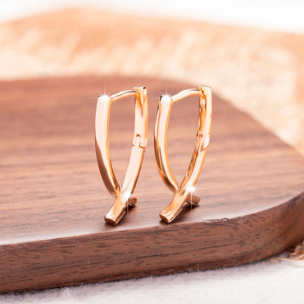 Rose gold coloured cross shaped earrings made from copper metal on a white background.