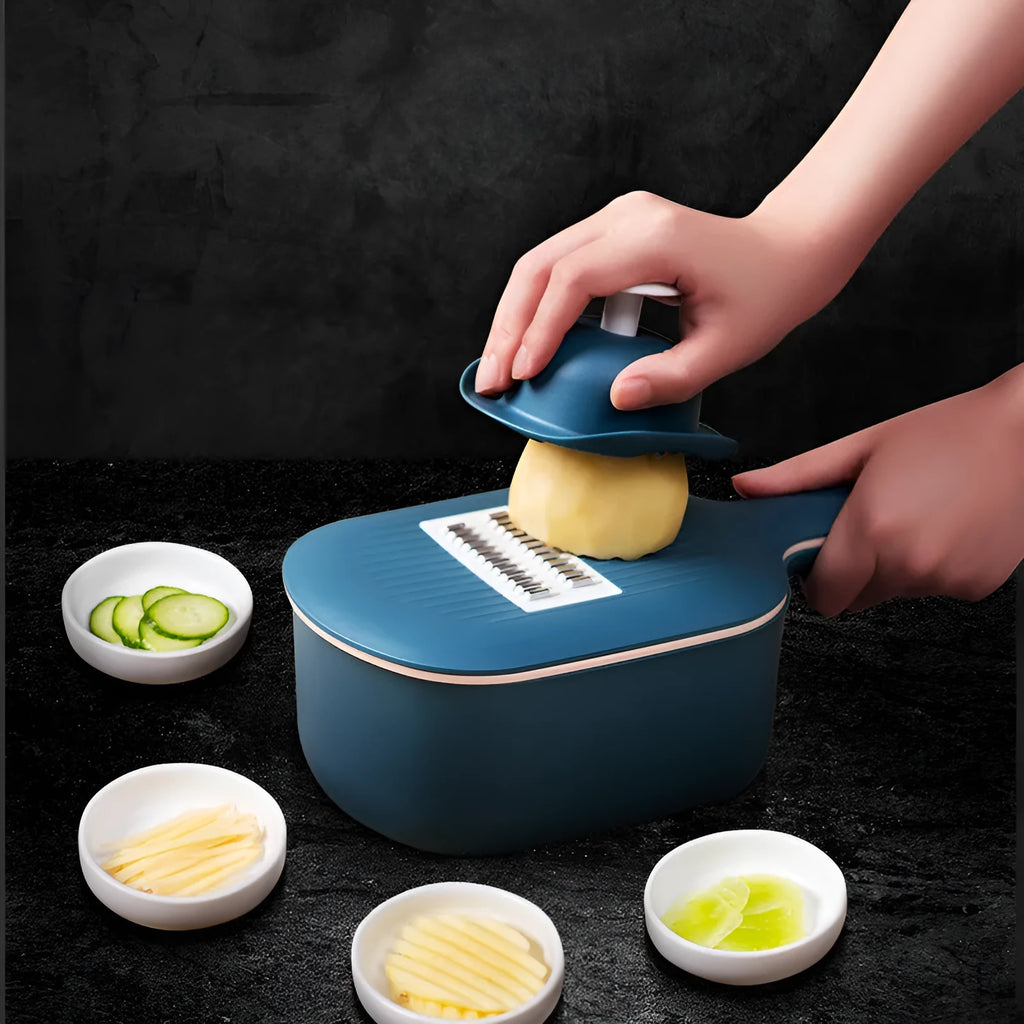 Dark blue vegetable cutter with four stainless steel blades, drain basket, and hand guard on a kitchen worktop