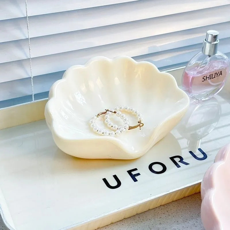 A white or pink plastic shell-shaped soap dish for bathroom counter or shower use.