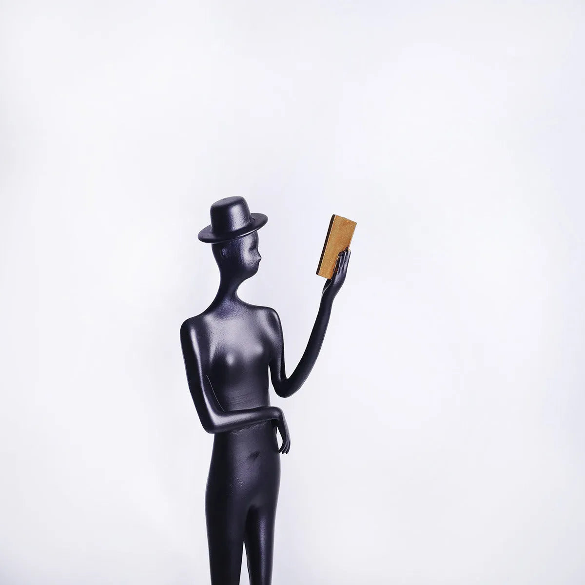 Black minimalist cast aluminum sculpture of a woman reading, 51cm tall on a desktop.