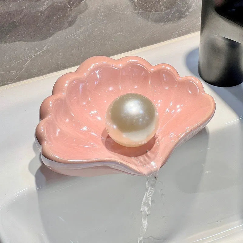A white or pink plastic shell-shaped soap dish for bathroom counter or shower use.