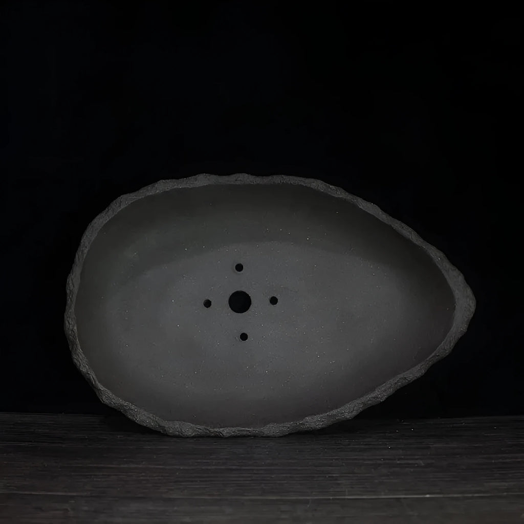 Handmade purple clay flower pot with drainage hole on a wooden floor