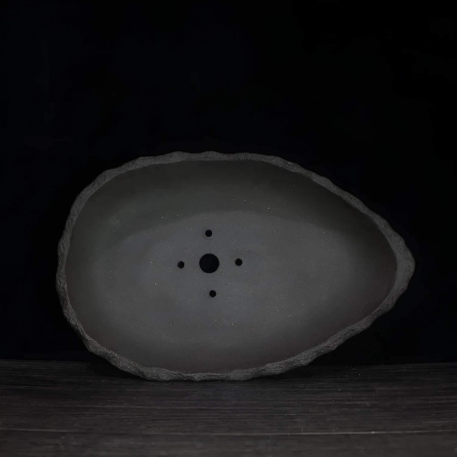 Handmade purple clay flower pot with drainage hole on a wooden floor