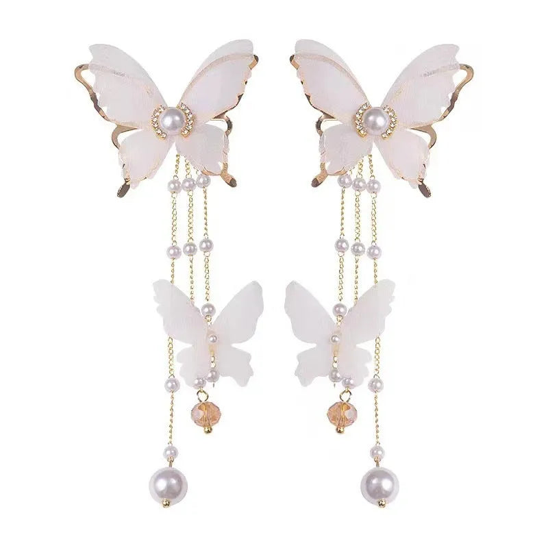 A pair of white butterfly-shaped earrings with pearls, rhinestones, and lace tassels on a copper alloy base.