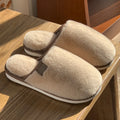 A pair of solid-colour plush winter slippers with a non-slip PVC sole on a wooden floor.