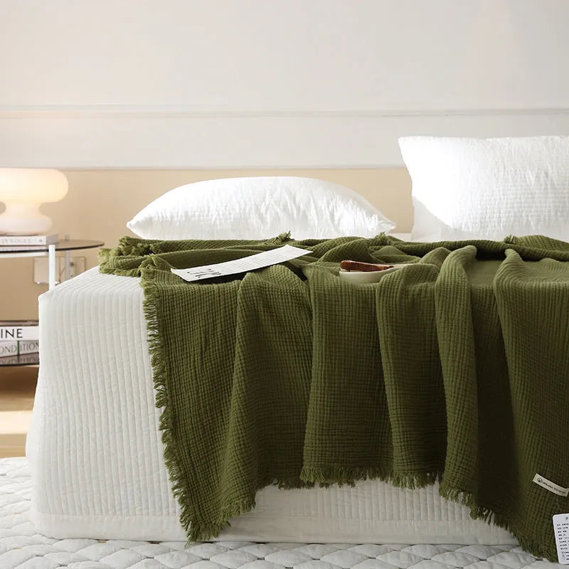 Four-layer gauze cotton blanket with tassel trim in avocado green, laid flat.