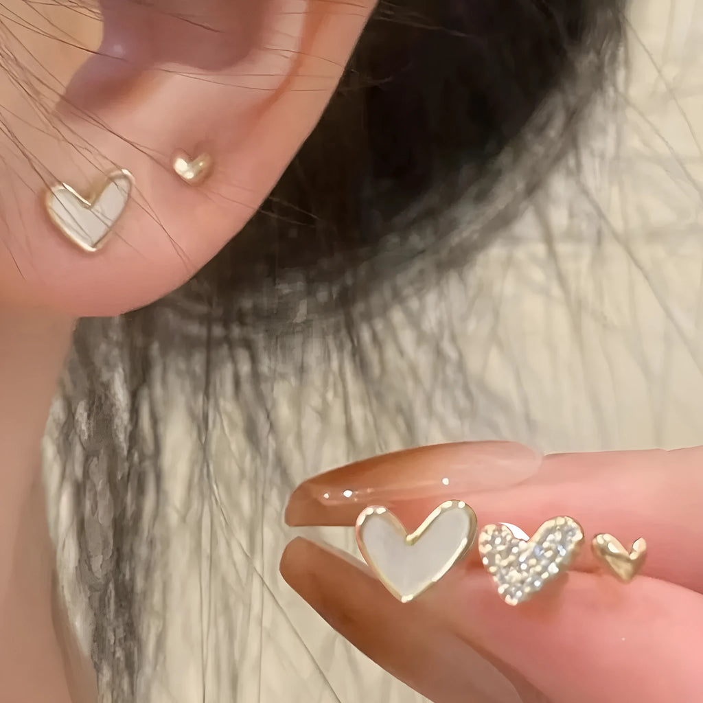 Three pairs of heart-shaped alloy earrings in gold, black, black and white, and pink colours on display.