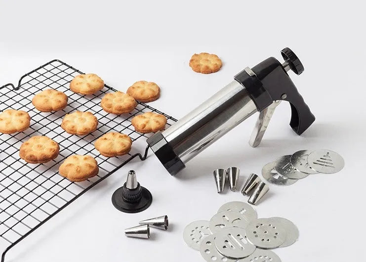 Stainless steel biscuit press gun with set of cookie moulds and piping nozzles on baking tray