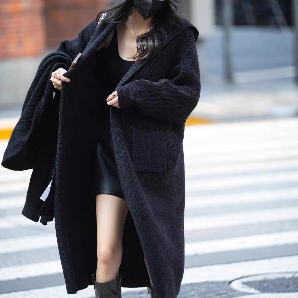 Long grey knitted hooded cardigan coat with long sleeves on a hanger.