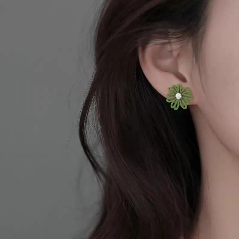 Close-up of colourful alloy flower stud earrings showing white and green two-tone design.