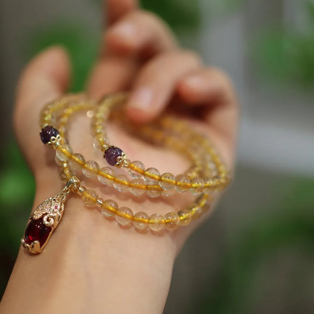 Handmade natural gold rutilated quartz bracelet with three gold circles and a chopsticks charm on a white background.