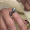 Geometric copper ring with black pearl and adjustable opening on a female index finger.