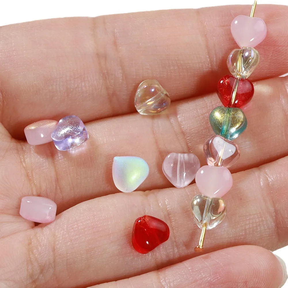 Twenty transparent love heart shaped spacer beads in assorted colours on a white background.