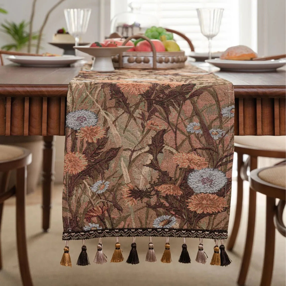 Beige jacquard table runner with floral pattern and long tassel fringes on a table.