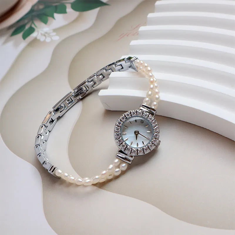 Women's light gold bracelet watch with natural freshwater pearls on a stainless steel strap, showing the 18mm round dial.