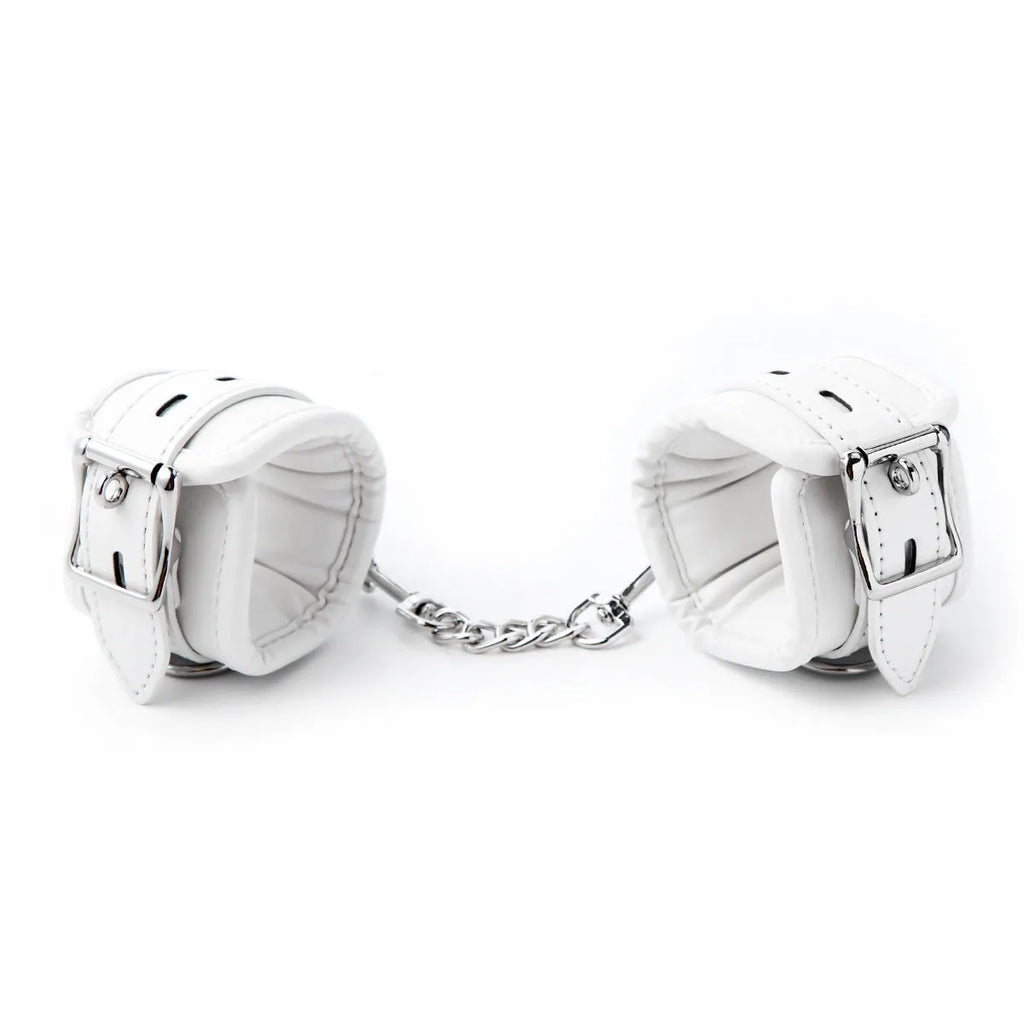 White PU sponge bondage restraint set showing handcuffs, foot cuffs, and a neck scarf on a dark surface.