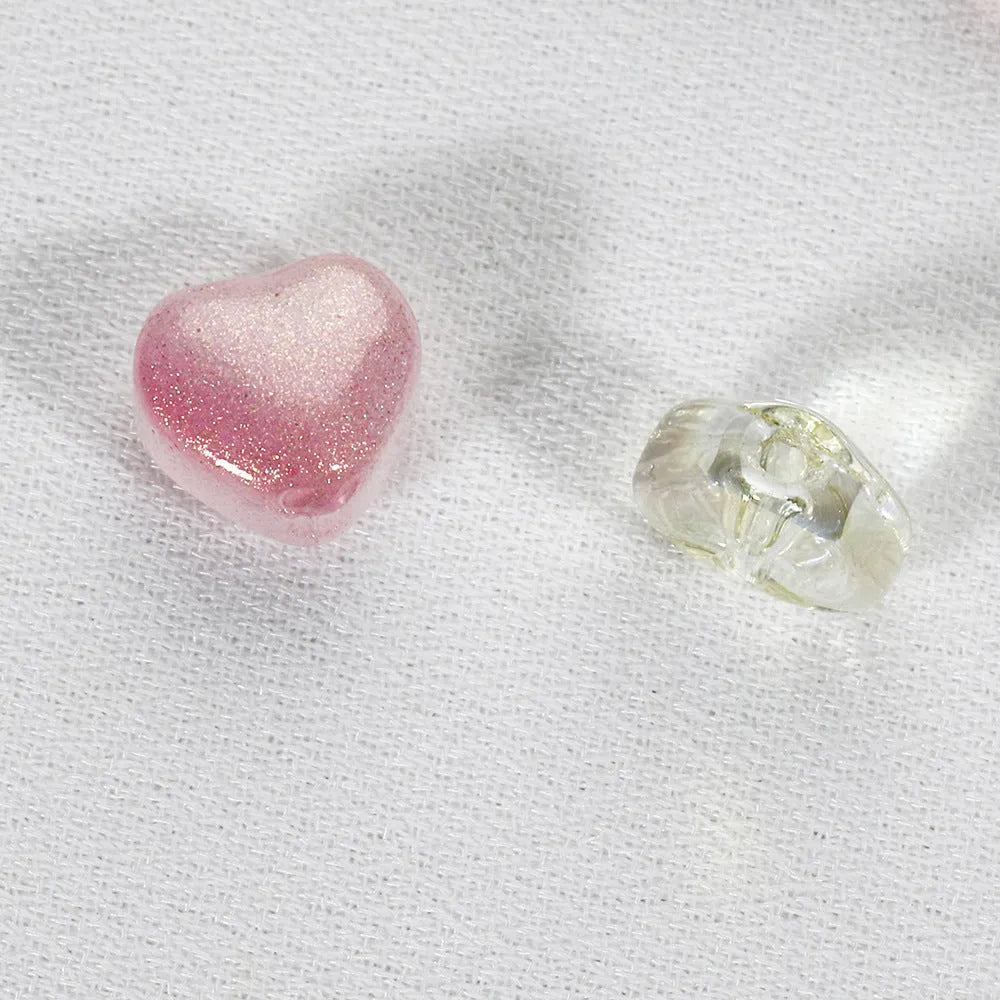 Twenty transparent love heart shaped spacer beads in assorted colours on a white background.