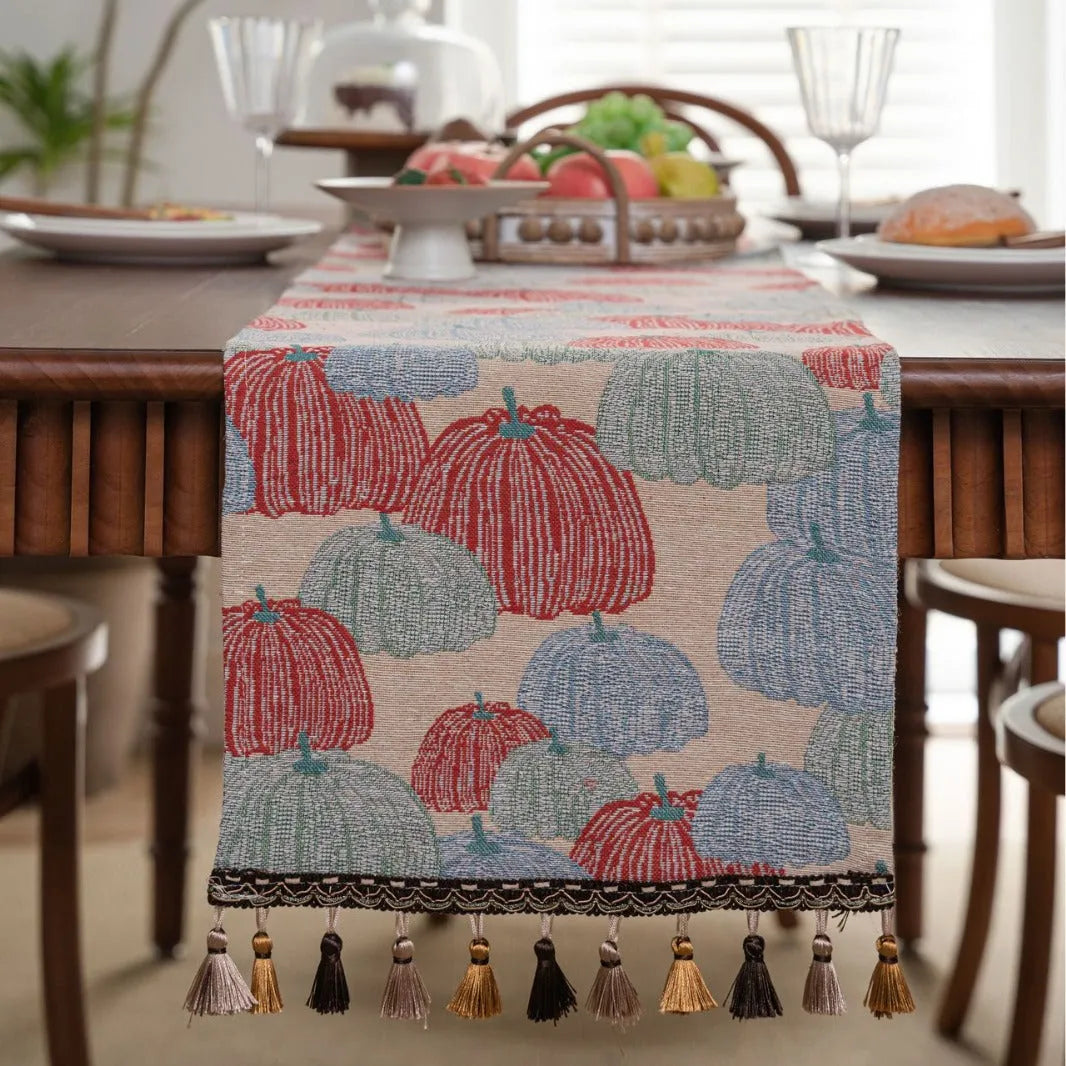 Beige jacquard table runner with floral pattern and long tassel fringes on a table.