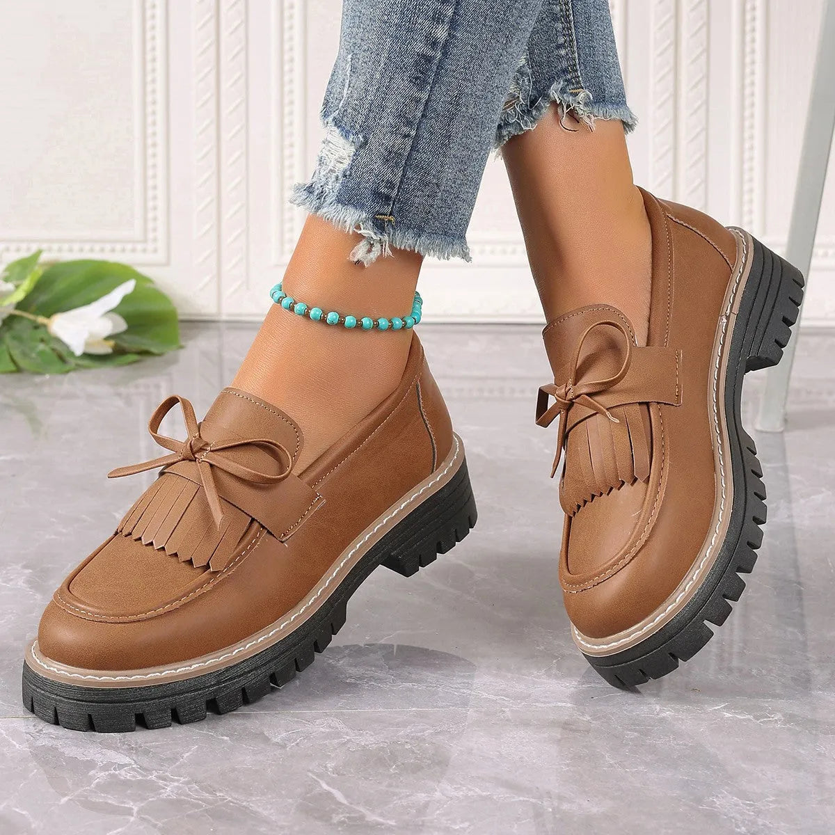 Women's black plus size loafers with tassel detail and a chunky rubber sole on a wooden floor.