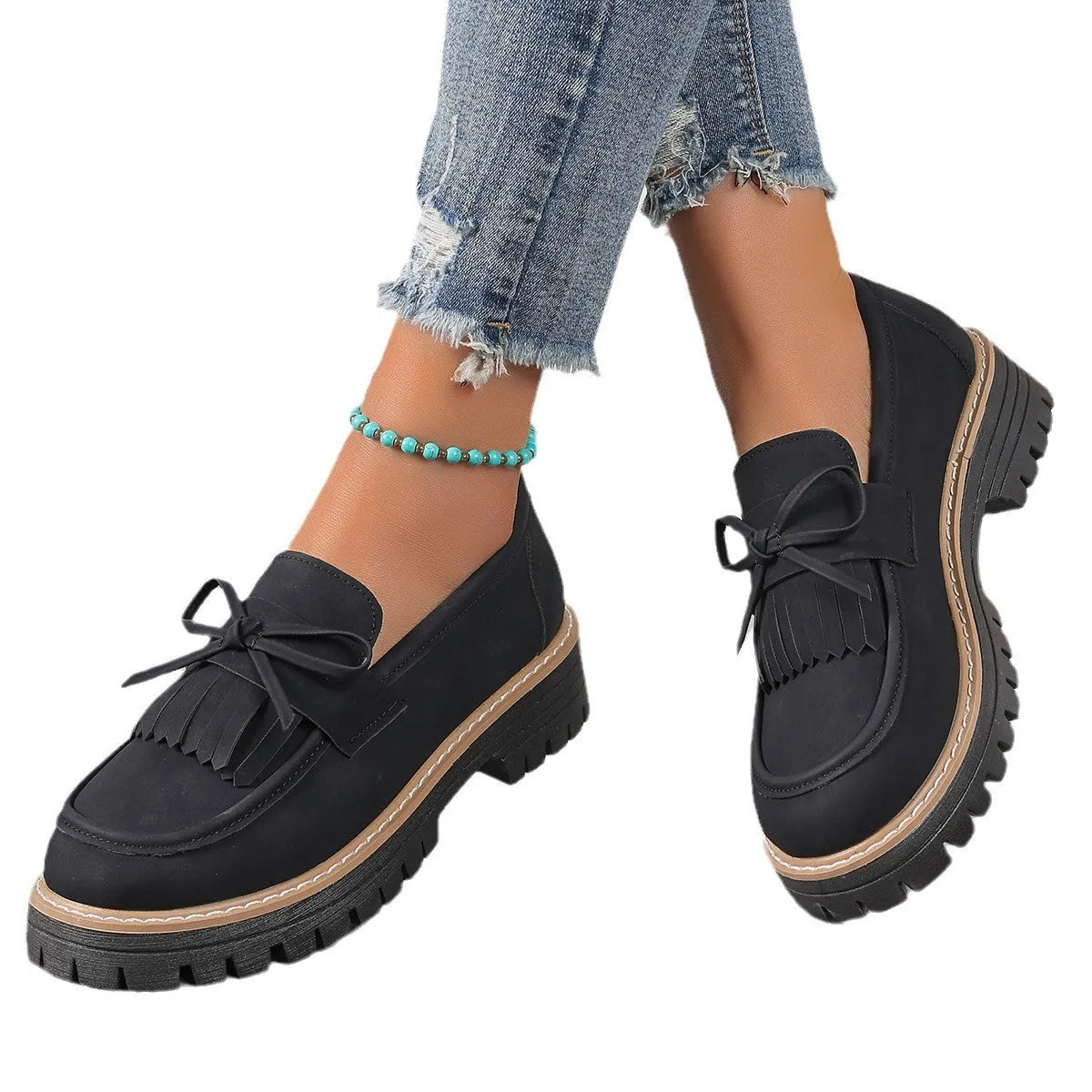 Women's black plus size loafers with tassel detail and a chunky rubber sole on a wooden floor.