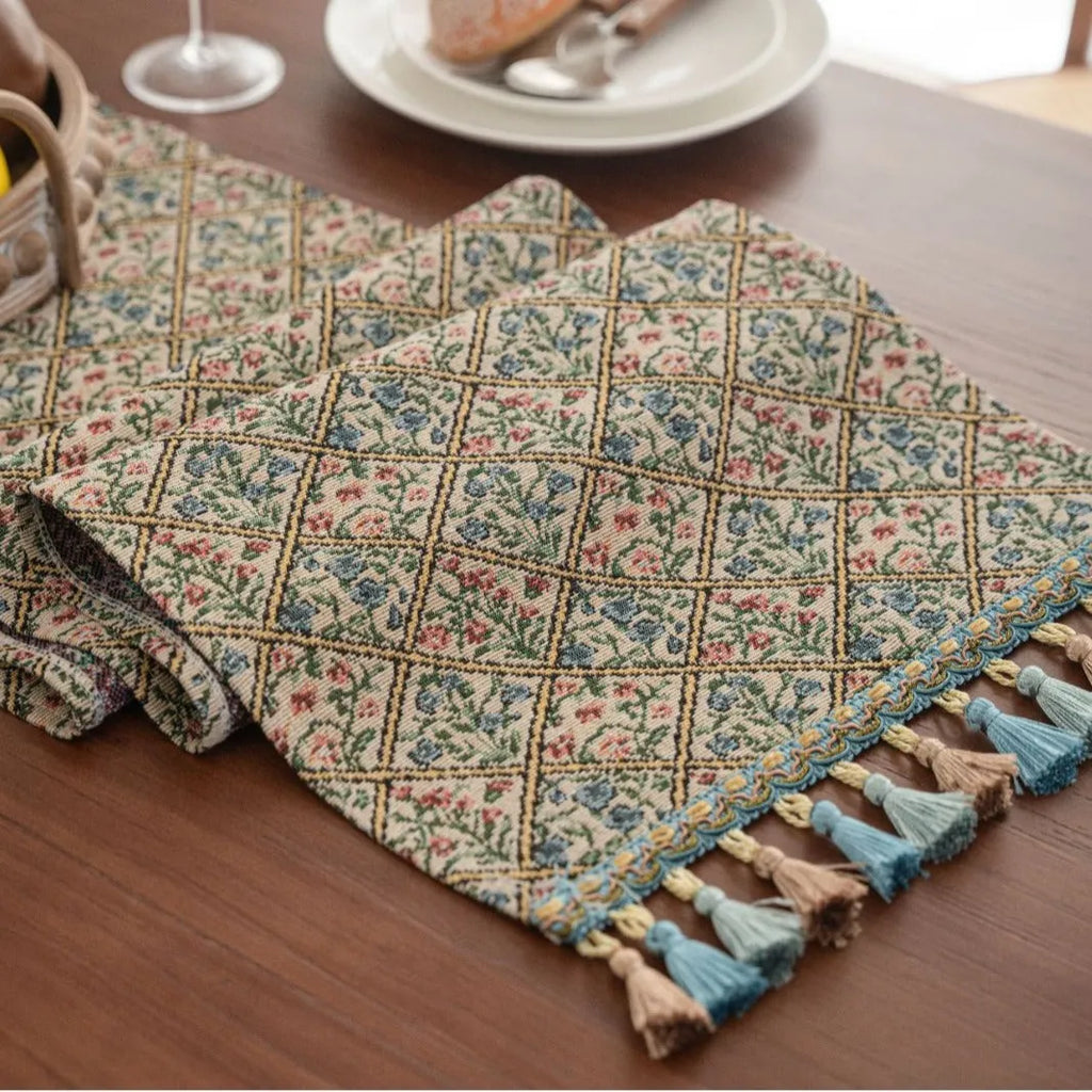Dark blue jacquard table runner with bouquet pattern and tassels laid on a wooden dining table.