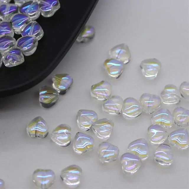 Twenty transparent love heart shaped spacer beads in assorted colours on a white background.
