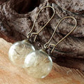 Close-up of a woman's ear wearing 16mm transparent glass ball dandelion seed earrings on a silver French hook.