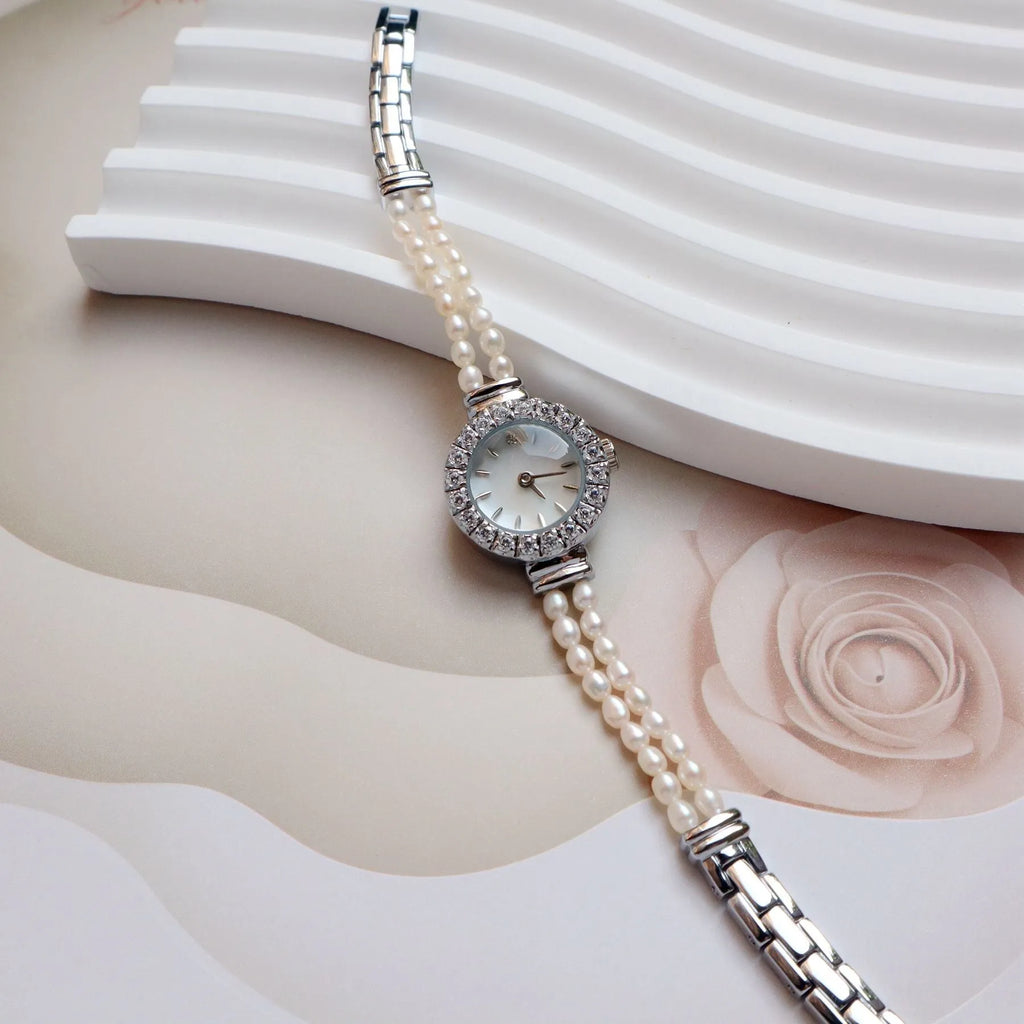 Women's light gold bracelet watch with natural freshwater pearls on a stainless steel strap, showing the 18mm round dial.