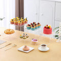 White and transparent plastic suit cube dessert display stands arranged in a tiered formation.