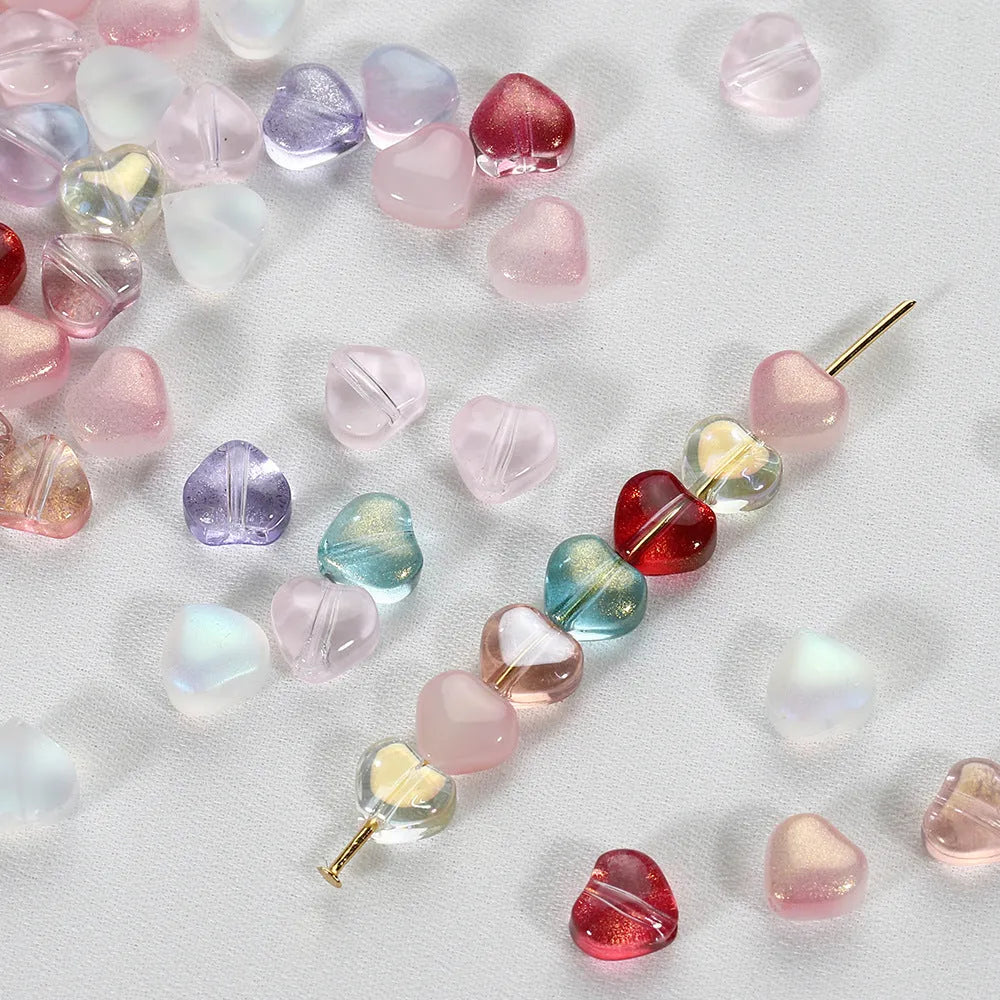 Twenty transparent love heart shaped spacer beads in assorted colours on a white background.