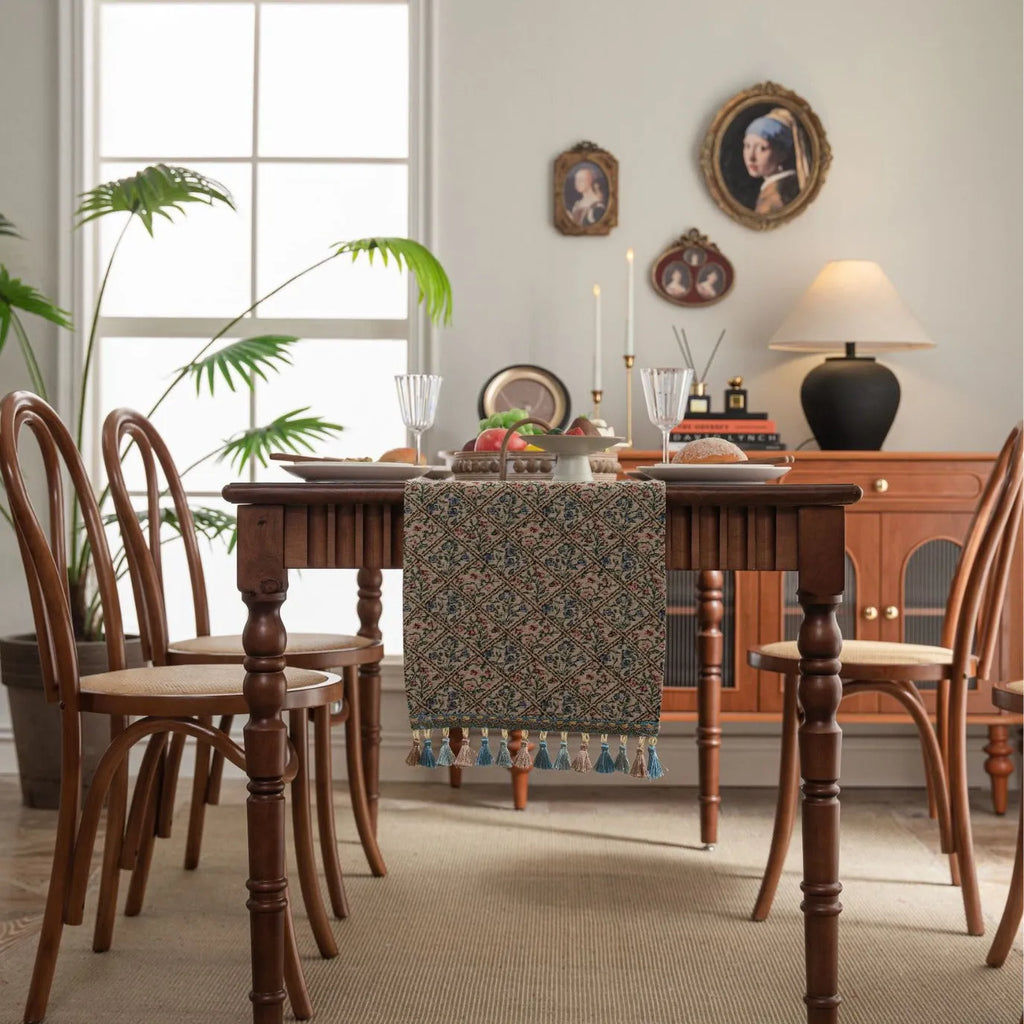 Dark blue jacquard table runner with bouquet pattern and tassels laid on a wooden dining table.