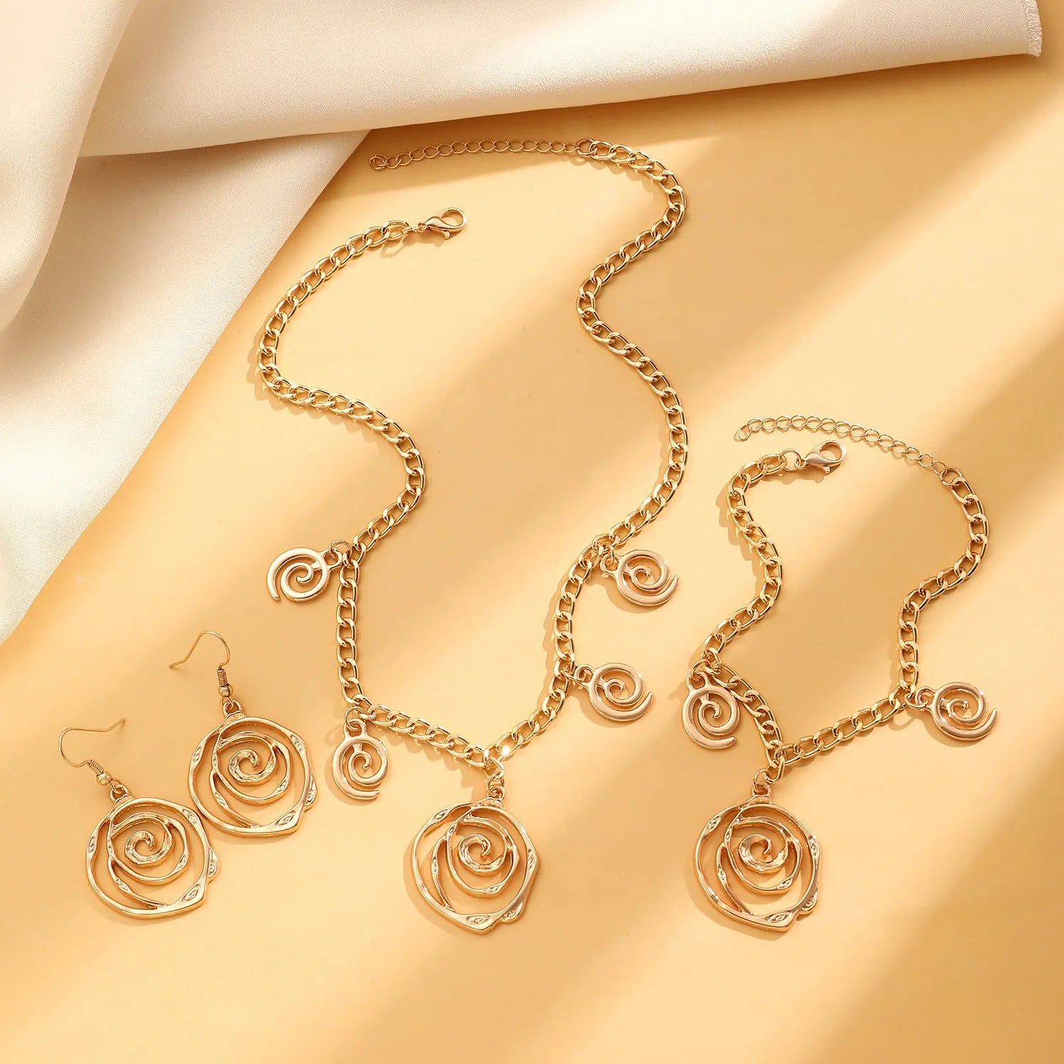 Spiral donut design women's jewellery set showing necklace, bracelet and ear hooks in gold or silver finish