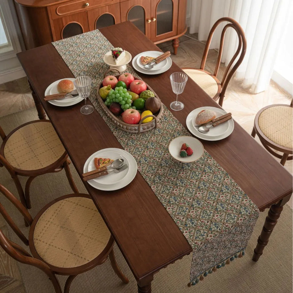 Dark blue jacquard table runner with bouquet pattern and tassels laid on a wooden dining table.